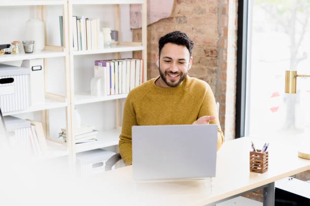 The young adult man uses his laptop to video conference with friends.